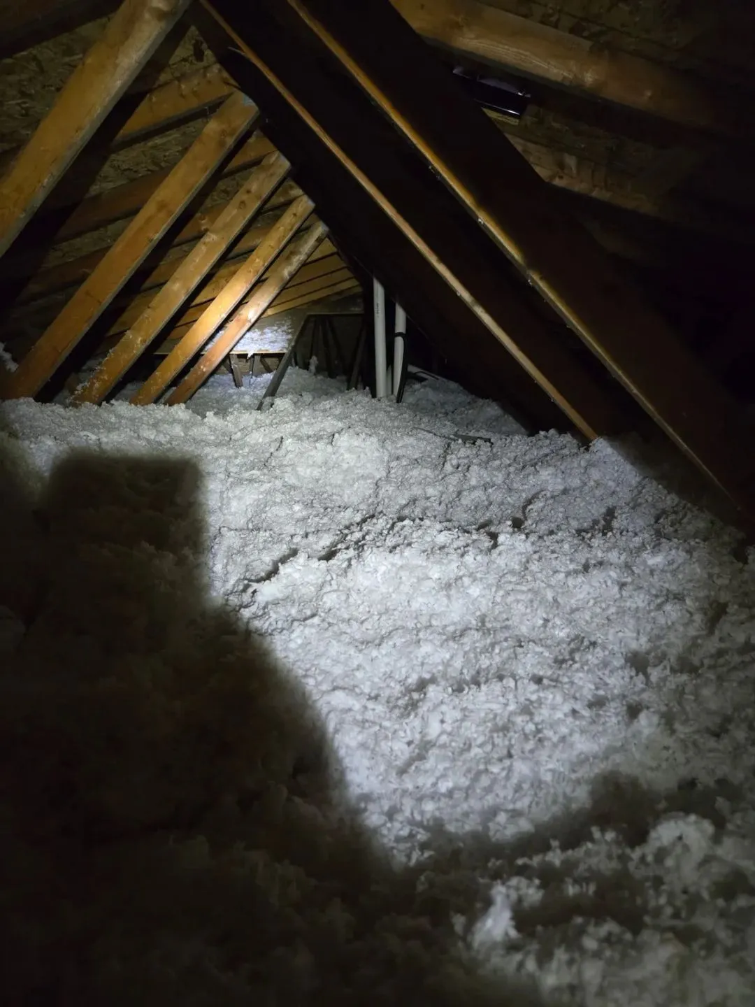 Flashlight illuminating insulation and structural details during an attic inspection